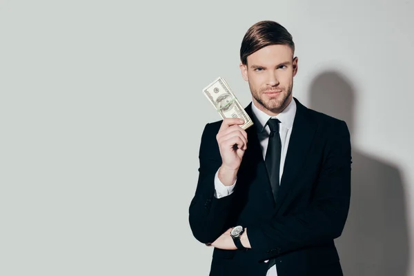 Young confident businessman in suit showing dollar banknote looking at camera on white background — Stock Photo