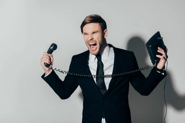 Homem de negócios irritado em terno gritando com telefone em mãos no fundo branco — Fotografia de Stock