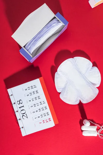 Vue du dessus des tampons menstruels, des doublures quotidiennes et du calendrier sur le rouge — Photo de stock