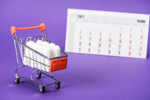 Tampões em carrinho de compras pequeno e calendário em roxo — Fotografia de Stock