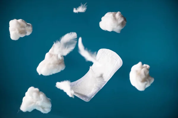 Falling daily pad and pieces of cotton with feathers isolated on blue — Stock Photo