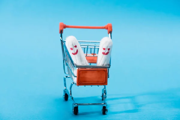 Dos tampones menstruales con emoticonos felices en un pequeño carrito de compras en azul - foto de stock