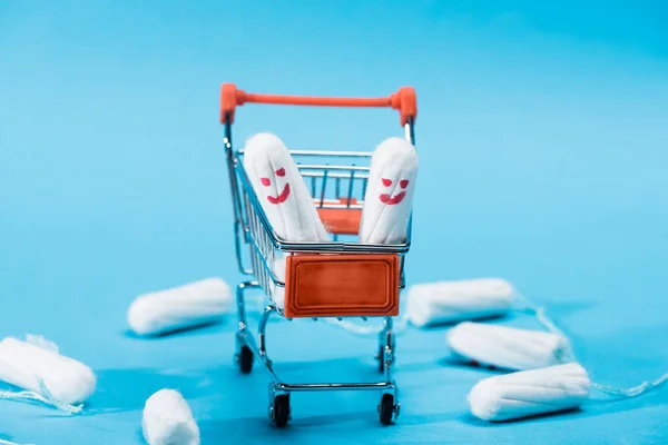 Assorbenti con faccine felici nel piccolo carrello della spesa blu — Foto stock