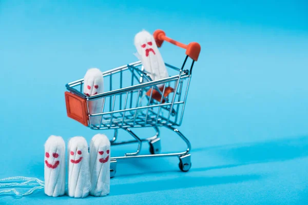 Tampons with happy and sad smileys in small shopping cart on blue — Stock Photo