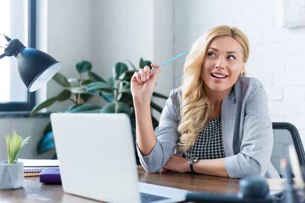 Усміхнена бізнес-леді тримає олівець і дивиться на роботу — стокове фото