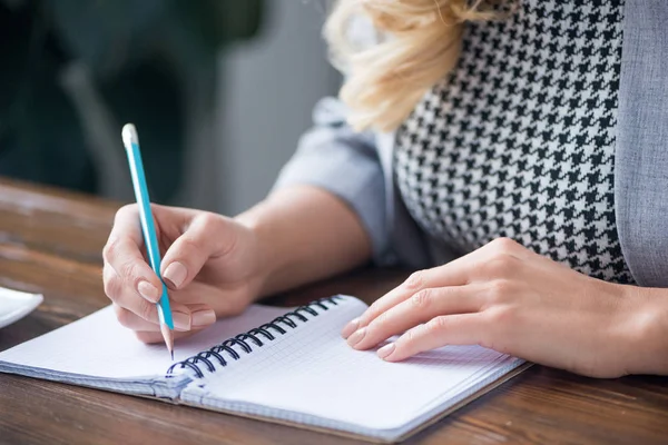 Imagen recortada de la mujer de negocios escribiendo algo a cuaderno con lápiz - foto de stock