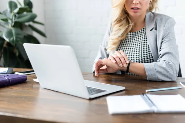 Abgeschnittenes Bild einer Geschäftsfrau, die auf Uhr im Büro mit Laptop schaut — Stockfoto