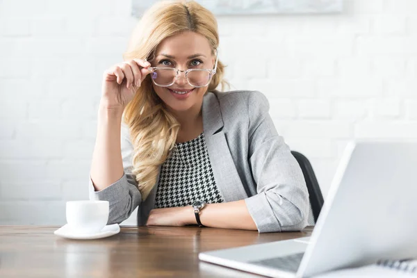 Lächelnde Geschäftsfrau blickt in Kamera über Brille — Stockfoto