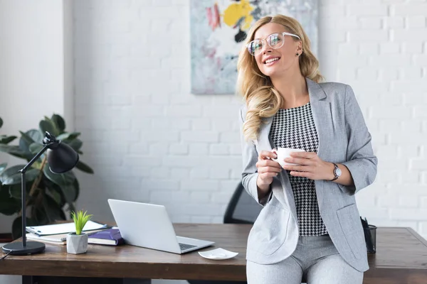 Усміхнена бізнес-леді тримає чашку кави в офісі — стокове фото