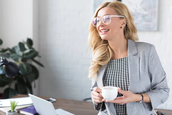 Smiling businesswoman holding cup of coffee and looking away — Stock Photo