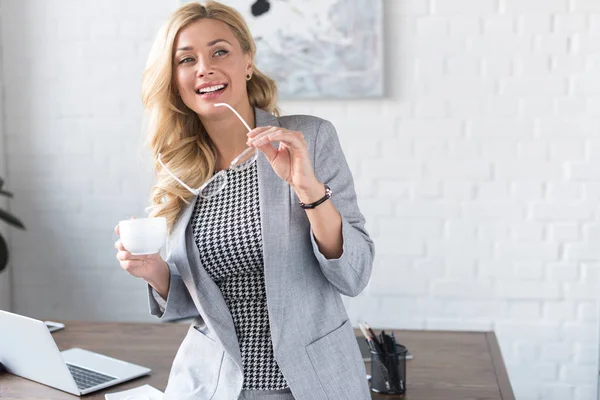 Улыбающаяся деловая женщина с чашкой кофе и стаканами — стоковое фото
