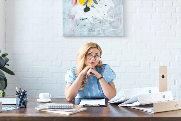 Pensive businesswoman sitting at table and looking up — Stock Photo