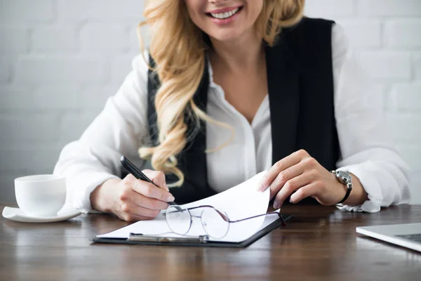 Cropped image of businesswoman writing something to clipboard at office — Stock Photo