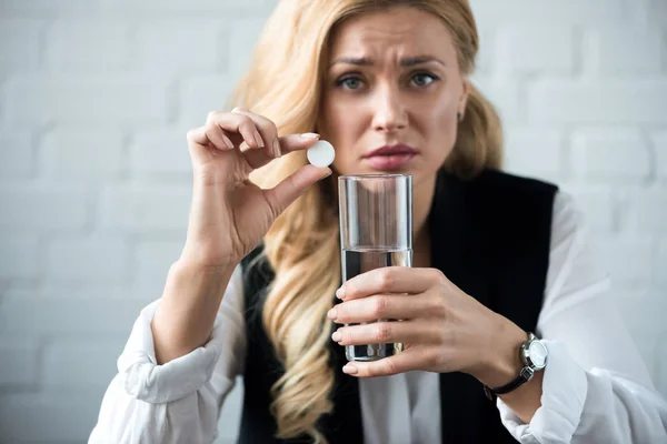 Деловая женщина держит таблетки и стакан воды и смотрит в камеру — стоковое фото