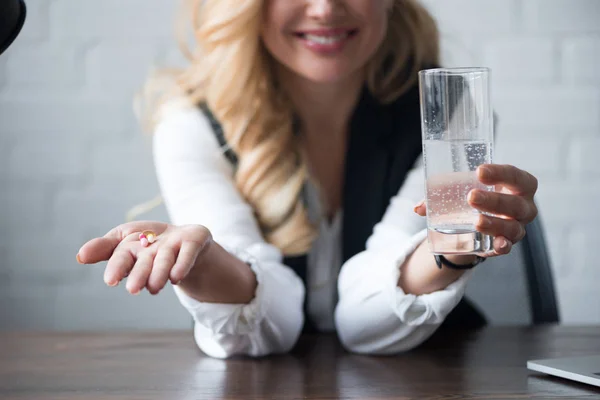 Cropped image of happy businesswoman holding pills and glass of water — Stock Photo