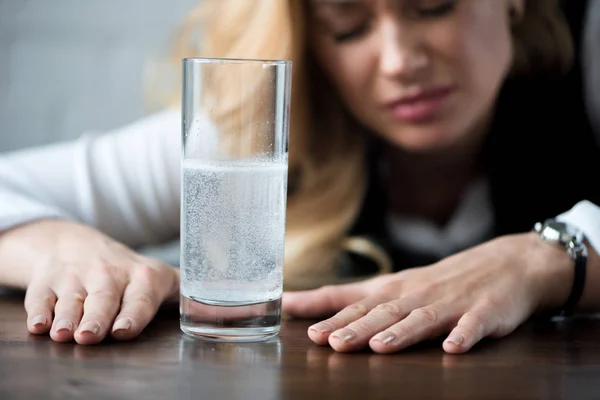 Donna d'affari con mal di testa seduta vicino a bicchiere d'acqua con medicinali — Foto stock