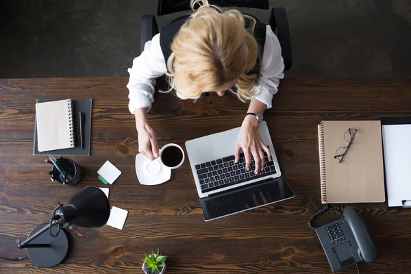 Vue du dessus de la femme d'affaires en utilisant un ordinateur portable et tenant une tasse de café au bureau — Photo de stock