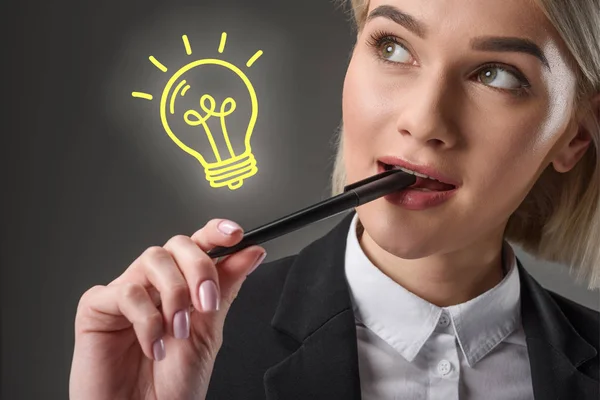 Portrait of beautiful young businesswoman with pen and light bulb symbol, isolated on grey — Stock Photo