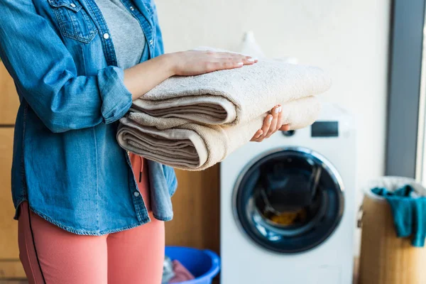 Tiro recortado de mujer joven sosteniendo toallas limpias apiladas en casa - foto de stock
