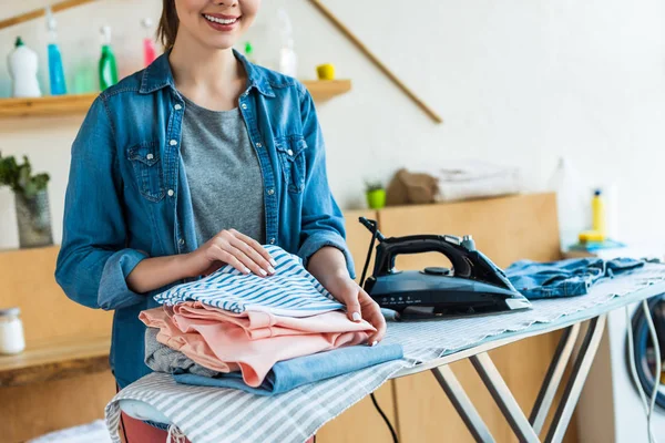 Tiro recortado de sorrir jovem mulher empilhando roupas depois de passar em casa — Fotografia de Stock