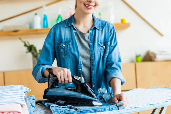 Abgeschnittene Aufnahme einer schönen lächelnden jungen Frau, die zu Hause Kleidung bügelt — Stockfoto