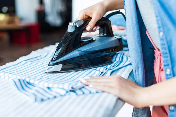 Primo piano vista parziale di giovane donna stiratura vestiti a casa — Foto stock