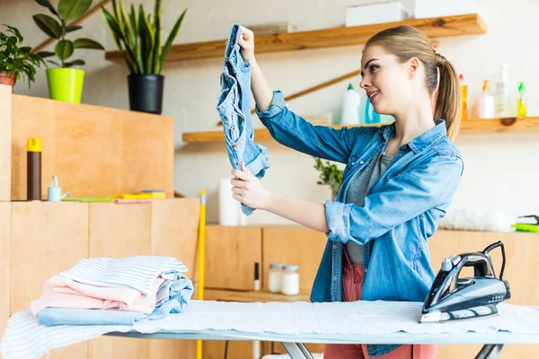 Bella sorridente giovane donna stiratura vestiti a casa — Foto stock