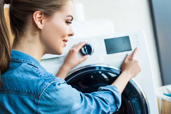 Belle jeune femme souriante utilisant une machine à laver à la maison — Photo de stock