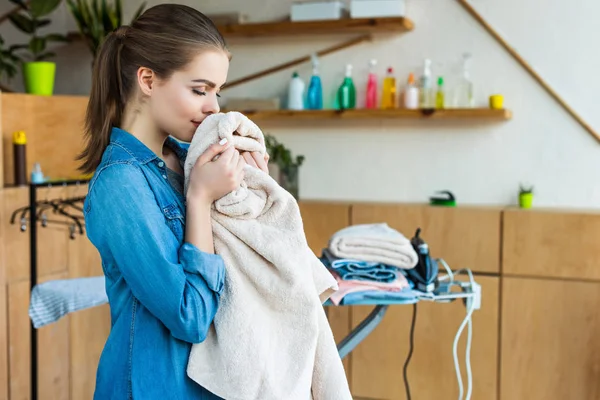 Smiling young woman holding towel while ironing clothes at home — Stock Photo