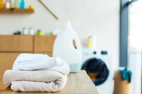 Vista ravvicinata di asciugamani puliti impilati e contenitore di plastica con fluido detergente sul tavolo di legno a casa — Foto stock