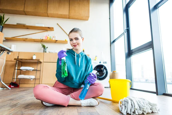 Bella giovane donna sorridente in guanti di gomma in possesso di bottiglie di plastica con liquidi detergenti — Foto stock