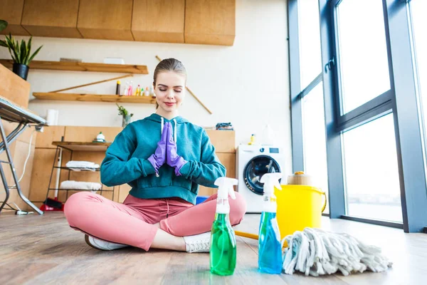 Schöne junge Frau sitzt auf dem Boden und meditiert, während sie das Haus putzt — Stockfoto