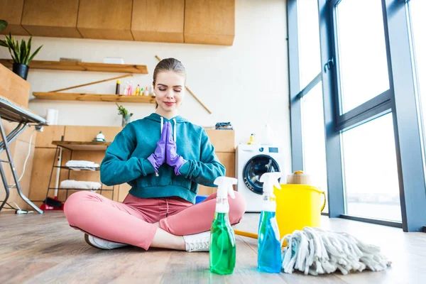 Hermosa joven sentada en el suelo y meditando mientras limpia la casa - foto de stock