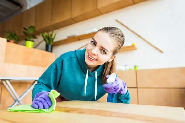 Schöne junge Frau lächelt in die Kamera, während sie zu Hause mit Lappen putzt — Stockfoto