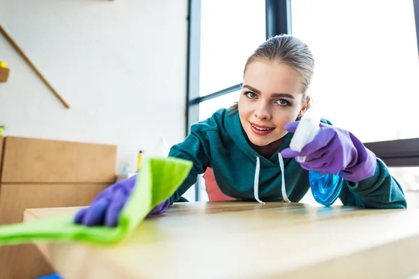 Young woman smiling at camera while cleaning home with rag — Stock Photo