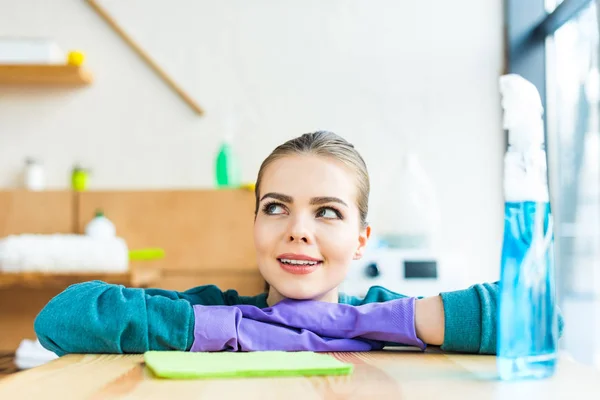 Souriant jeune femme en gants de caoutchouc regardant loin à la maison — Photo de stock