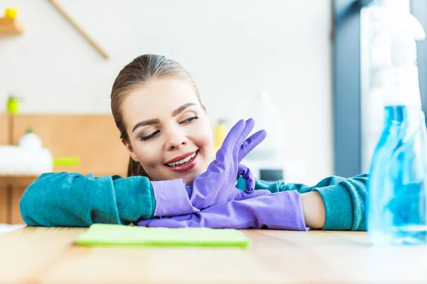 Sonriente joven con guantes de goma mientras limpia la casa - foto de stock