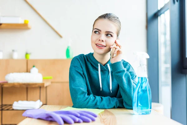 Mujer joven y feliz hablando por teléfono inteligente mientras limpia la casa - foto de stock