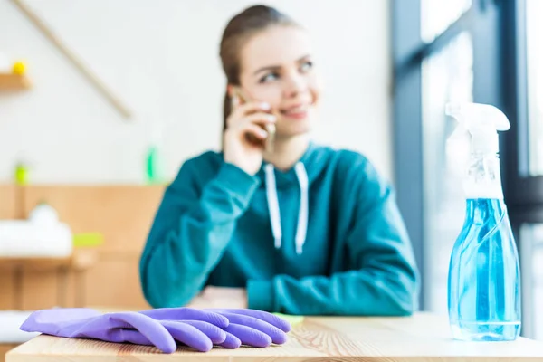 Smiling young woman talking by smartphone while cleaning house — Stock Photo