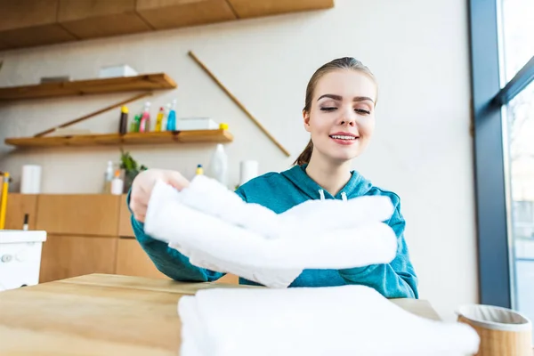 Sorrindo jovem mulher empilhando toalhas brancas limpas na mesa — Fotografia de Stock