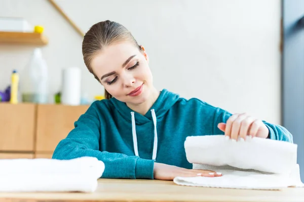 Smiling young woman looking at white towels on table — Stock Photo