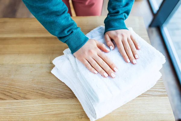 Cropped shot of female hands and clean white towels on wooden table — Stock Photo