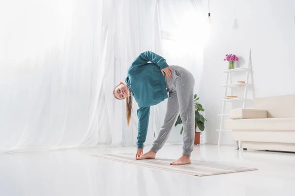 Chica estiramiento en yoga mat en casa - foto de stock