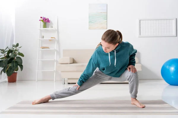 Chica estirando piernas en yoga estera en casa - foto de stock