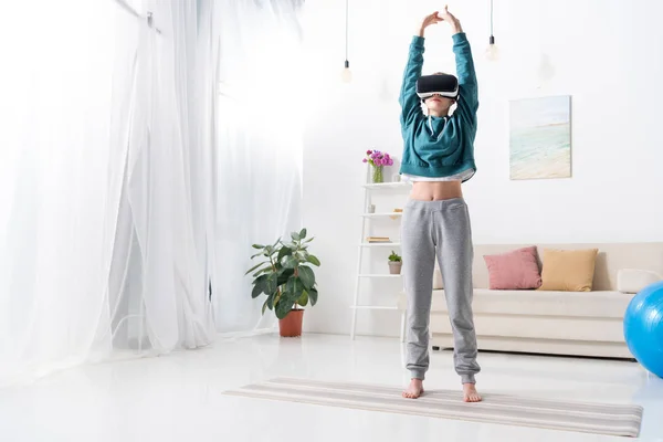 Chica haciendo yoga con auriculares de realidad virtual en alfombra de yoga en casa - foto de stock
