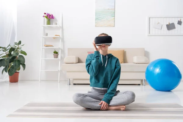 Девушка сидит в позе лотоса с гарнитурой виртуальной реальности дома — стоковое фото