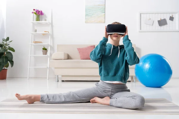 Sportive girl stretching with virtual reality headset on yoga mat at home — Stock Photo