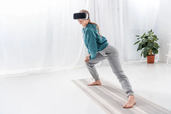 Chica estiramiento piernas con vr auriculares en yoga estera en casa - foto de stock