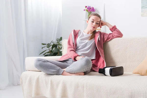 Chica cansada sentada en el sofá y sosteniendo el teléfono inteligente en casa - foto de stock