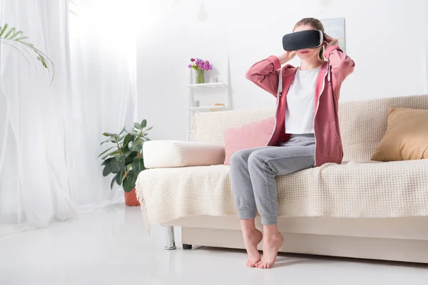 Девушка в гарнитуре виртуальной реальности на диване дома — стоковое фото